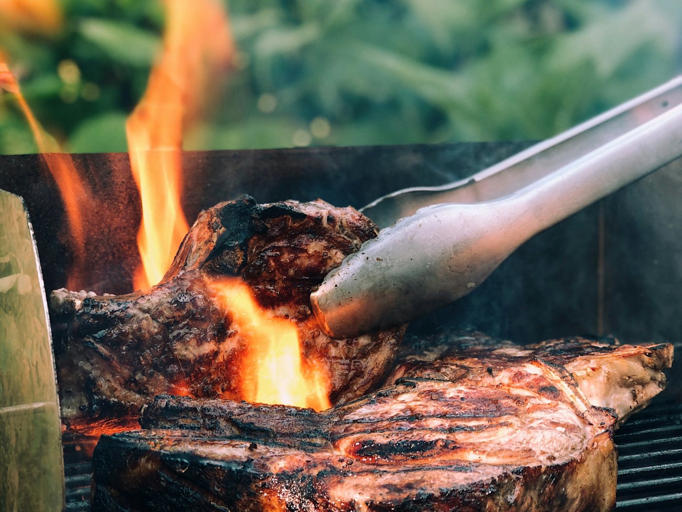 Carne sobre la parrilla con llamas altas y unas pinzas de cocina